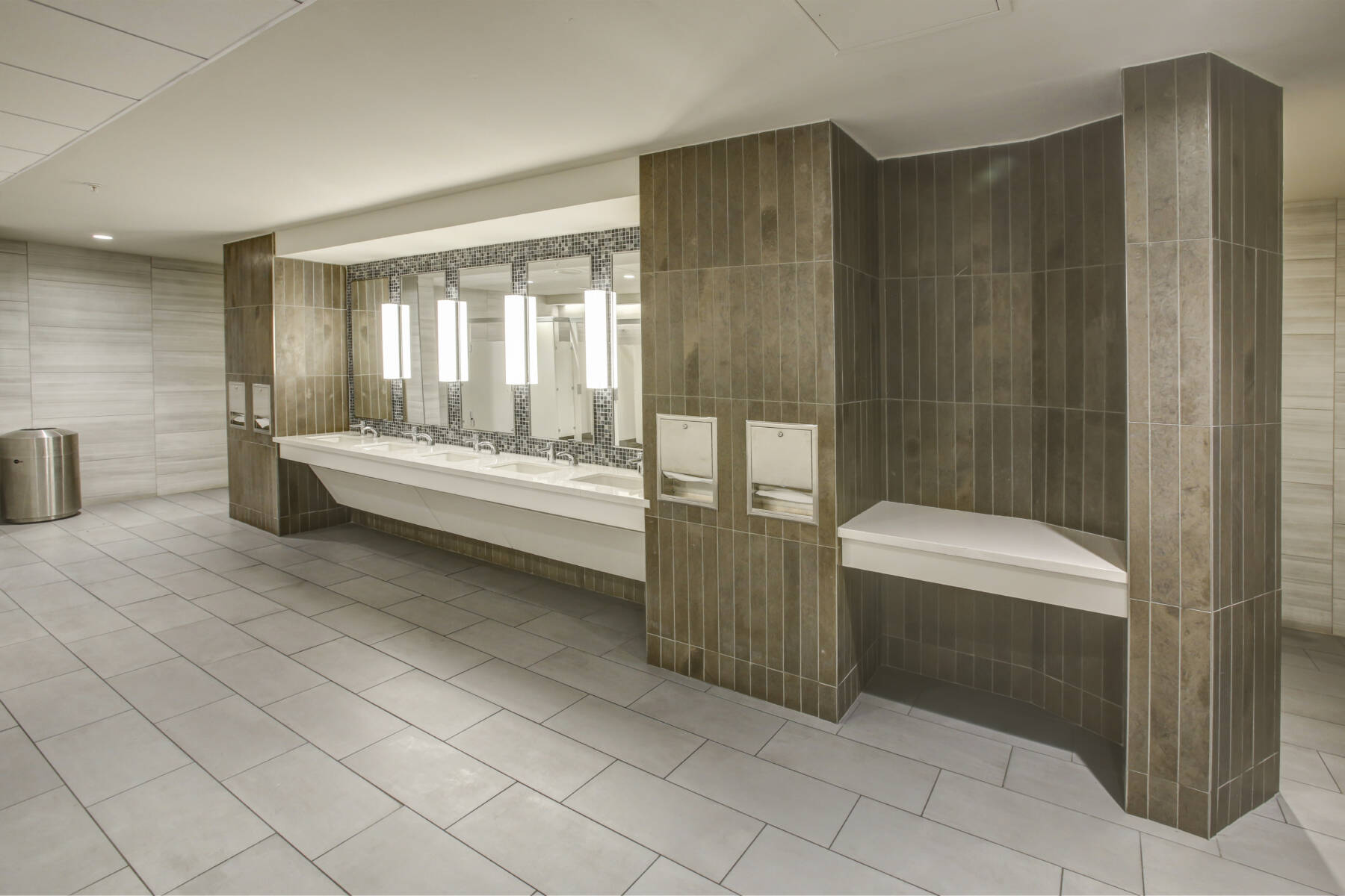 Handwashing station in a restroom with white tile flooring and brown wall tile. This image demonstrates this company's excellence in multi-purpose sports flooring installations.
