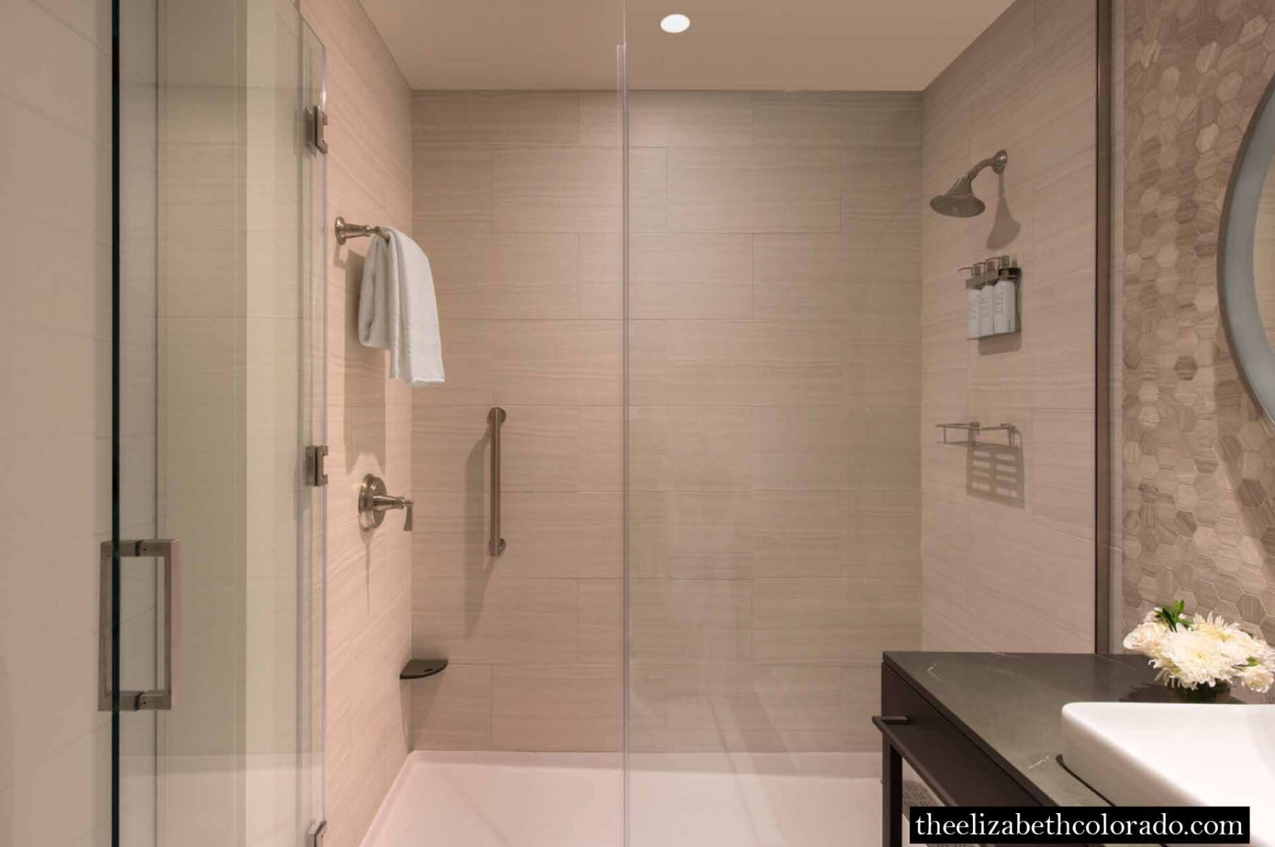 Spacious guest bathroom shower with soothing cream tile from floor to ceiling.